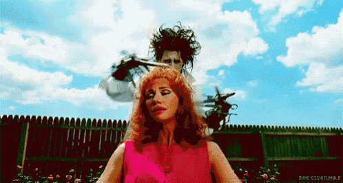 a woman in a pink shirt is getting her hair cut by a man with scissors in his hand