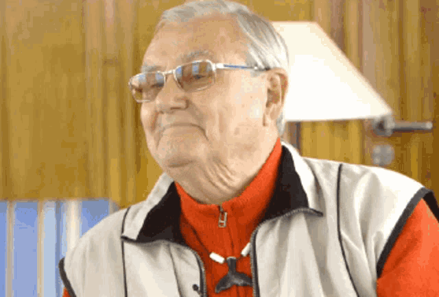 an elderly man wearing glasses and a red sweater is sitting in front of a lamp