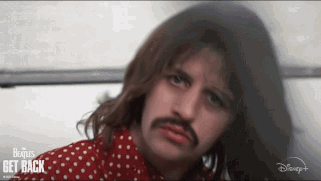 a man with long hair and a mustache is wearing a red and white polka dot shirt from the beatles get back