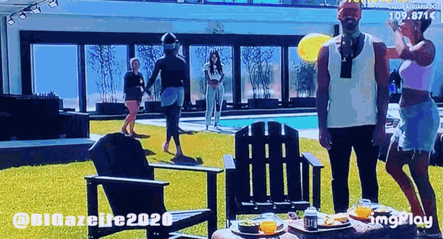 a group of people are standing in front of a swimming pool and a table with food and drinks on it