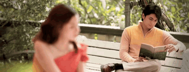a man is reading a book while a woman is sitting on a bench .