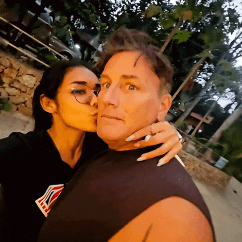 a woman kisses a man on the cheek while wearing a black shirt with the letter k on the front