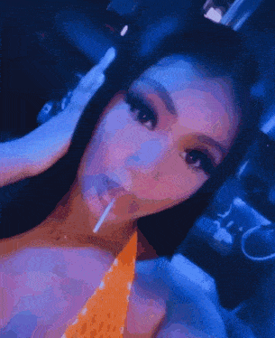 a woman in an orange top is smoking a cigarette in a dark room .