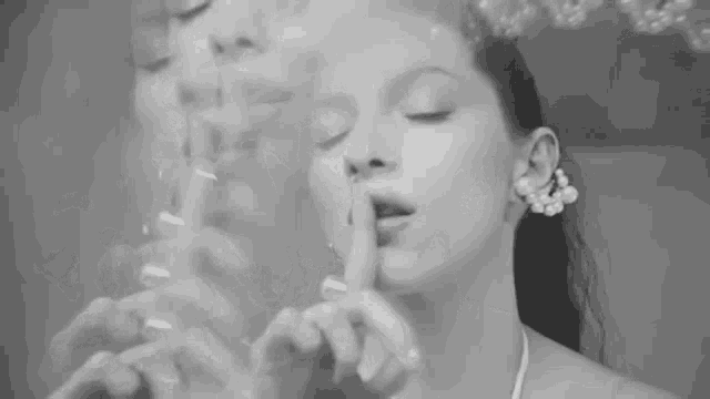 a black and white photo of a woman making a shhh gesture .