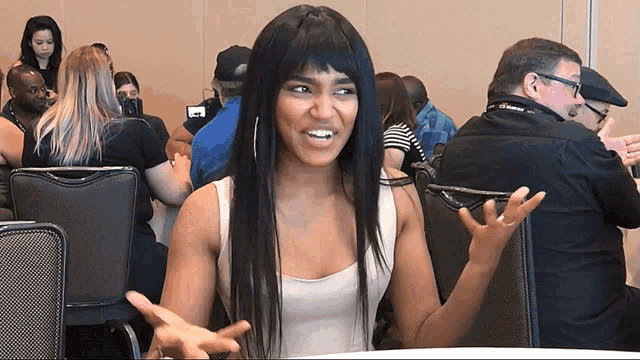 a woman in a white tank top is sitting at a table with her hands outstretched