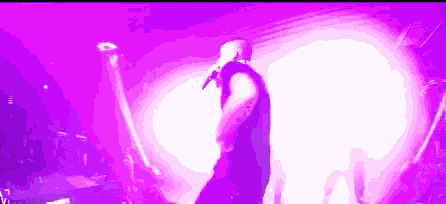 a man is singing into a microphone on a stage in front of a purple light .