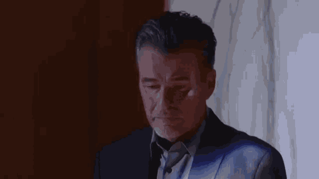 a man in a suit and tie is standing in front of a wall .