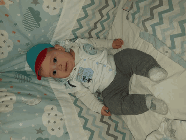 a baby is laying on a bed with a blanket that has clouds and stars