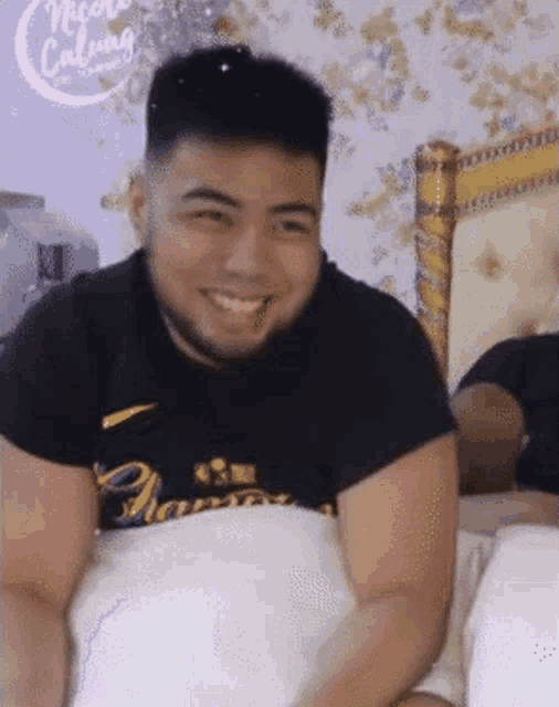 a man with a beard is smiling while laying on a bed with a sign that says more calming in the background