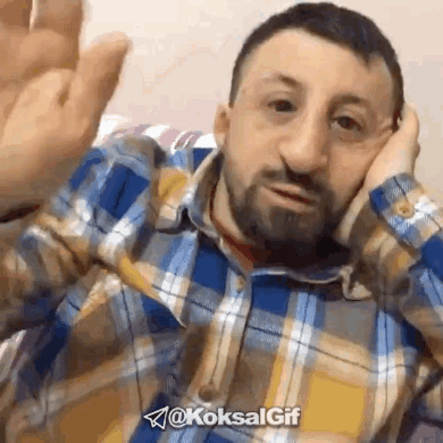 a man with a beard wearing a plaid shirt is waving his hand