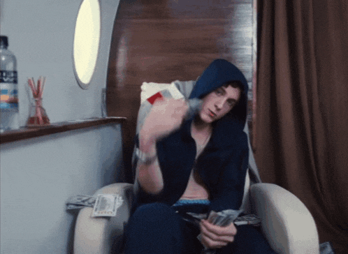 a man in a hoodie sits in a chair with a bottle of aquafina water behind him
