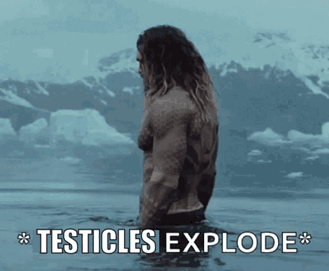 a man with long hair is standing in the water with the words testicles explode above him .
