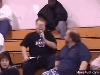 a man is holding a microphone while sitting in a bleacher .