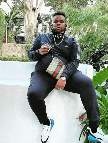 a man wearing a gucci bag sits on a white wall