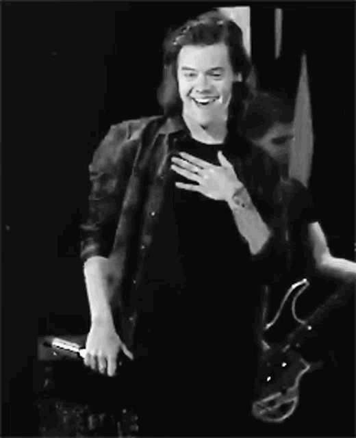 a black and white photo of a man with long hair smiling and holding his hand to his chest .