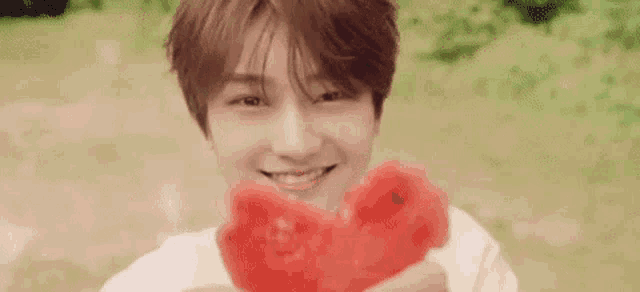 a young man is holding a slice of watermelon and smiling .