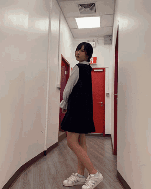 a woman is standing in a hallway with a red exit sign on the wall