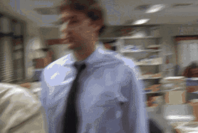 a blurry picture of a man in a blue shirt and tie in an office