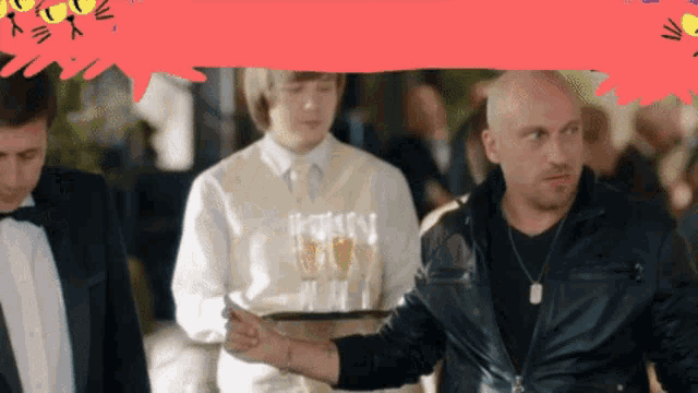 a man in a black jacket is holding a tray with two glasses of wine on it
