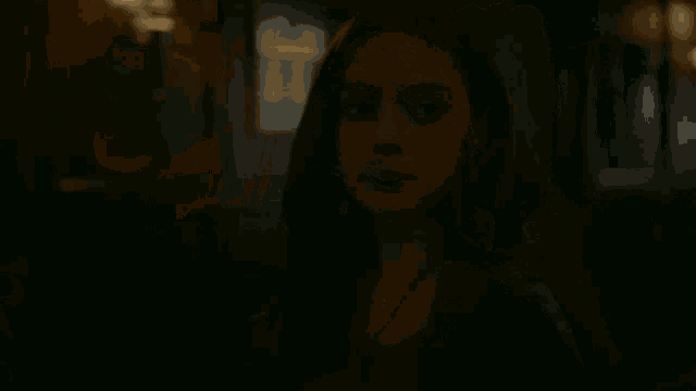 a woman in a dark room with a necklace around her neck looks down