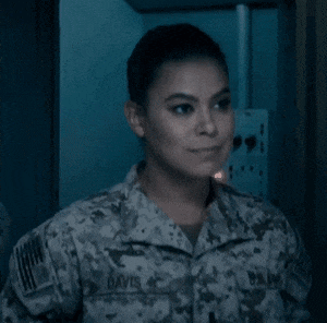 a woman in a military uniform is smiling while standing in a dark room .