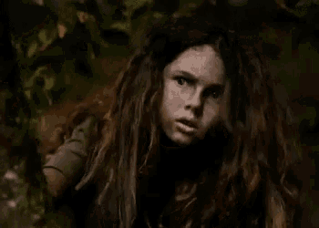 a young girl with long red hair is standing in the woods .