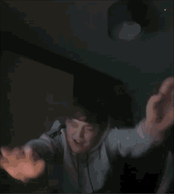 a person with their arms outstretched in a dark room with a green light on the ceiling