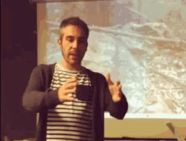 a man in a striped shirt is giving a presentation in front of a screen .