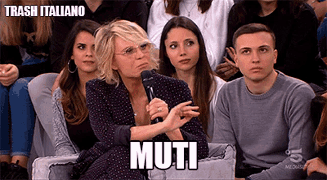 a group of people sitting on a couch with a woman holding a microphone and the word muti written above her