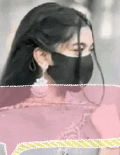 a woman wearing a black mask is standing in front of a pink background .