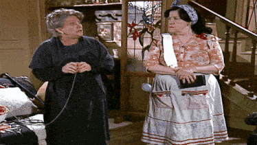 two older women are standing next to each other and one is knitting