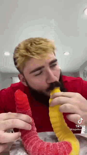 a man with a beard is eating a gummy worm shaped like a banana .