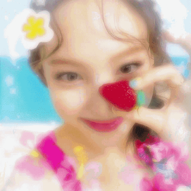 a woman is holding a strawberry in front of her nose .