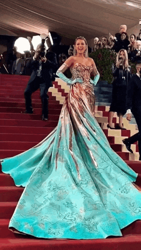 a woman in a long blue and gold dress is walking down stairs