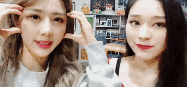two girls are making funny faces in front of a bookshelf