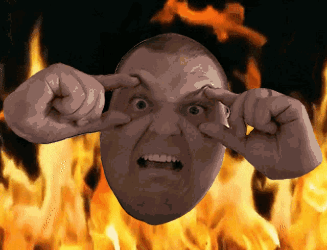 a man covering his eyes with his hands in front of a fire