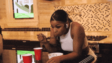 a woman in a white tank top is eating a bowl of food