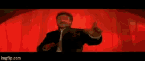 a man in a suit and tie is standing in front of a red curtain in a dark room .