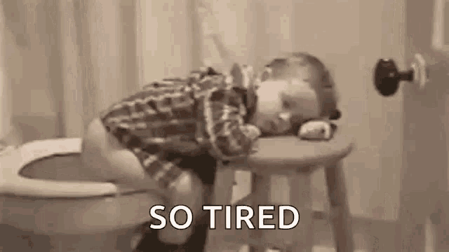 a baby is sleeping on a stool in a bathroom next to a toilet .