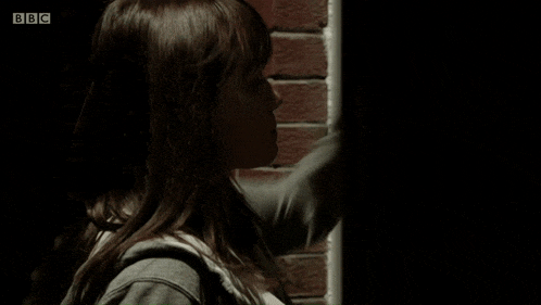 a woman is standing in front of a brick wall with bbc written on the bottom