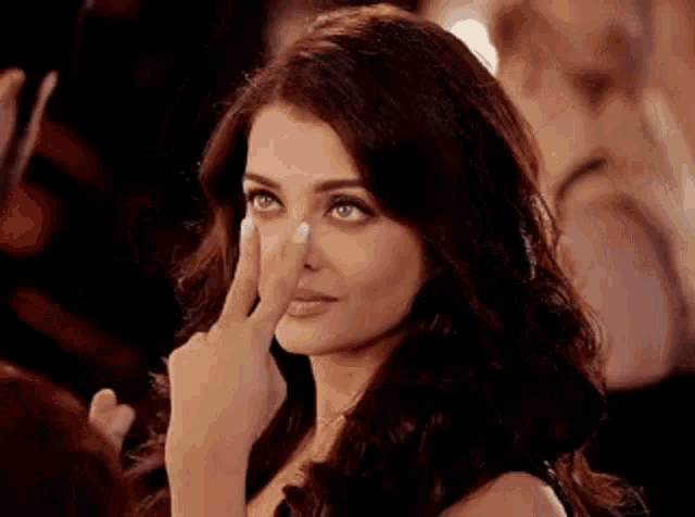 a woman is touching her nose with her finger while looking at the camera .