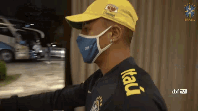 a man wearing a face mask and a yellow hat with the word itau on the sleeve
