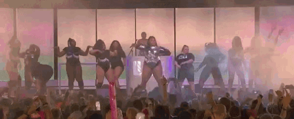 a group of women are dancing in front of a crowd with the word u.s. on the wall behind them