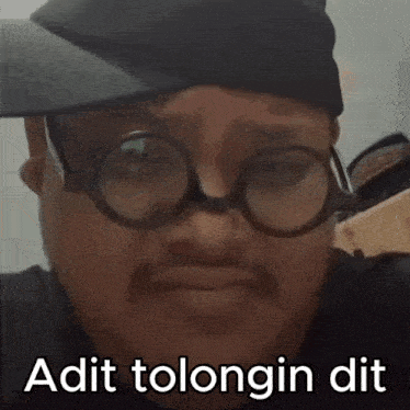 a man wearing glasses and a hat says " adit tolongin dit " on the bottom