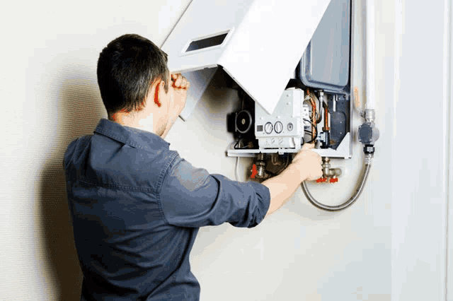 a man in a gray shirt is working on a boiler that has the number 100 on it