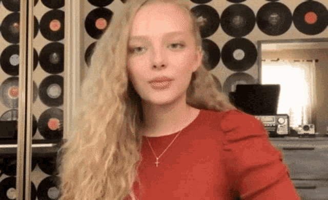 a woman in a red shirt and necklace is standing in front of a record wall .