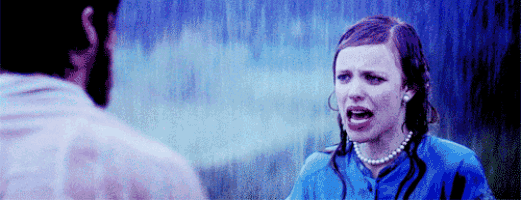 a woman in a blue shirt is screaming in the rain while a man looks on .