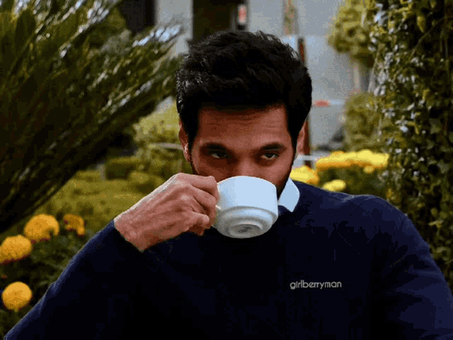 a man wearing a girlberryman sweater is drinking from a white cup