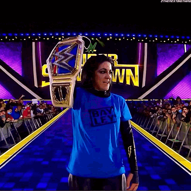 a woman in a blue shirt holds a wrestling championship belt in front of a sign that says super show