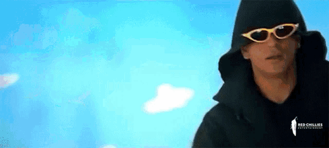 a man wearing sunglasses and a hooded jacket is standing in front of a blue sky .